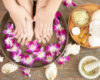 closeup view of woman soaking her hand and feet in dish with water and flowers on wooden floor. Spa treatment and product for female feet and hand spa. orchid flowers in ceramic bowl.